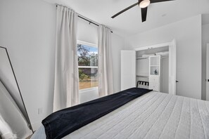 Un dormitorio con cama, una ventana con cortinas, un ventilador de techo y un armario.