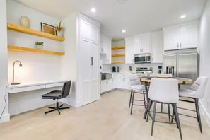 A modern kitchen with white cabinets, a dining area with white chairs, and a built-in desk with a chair.