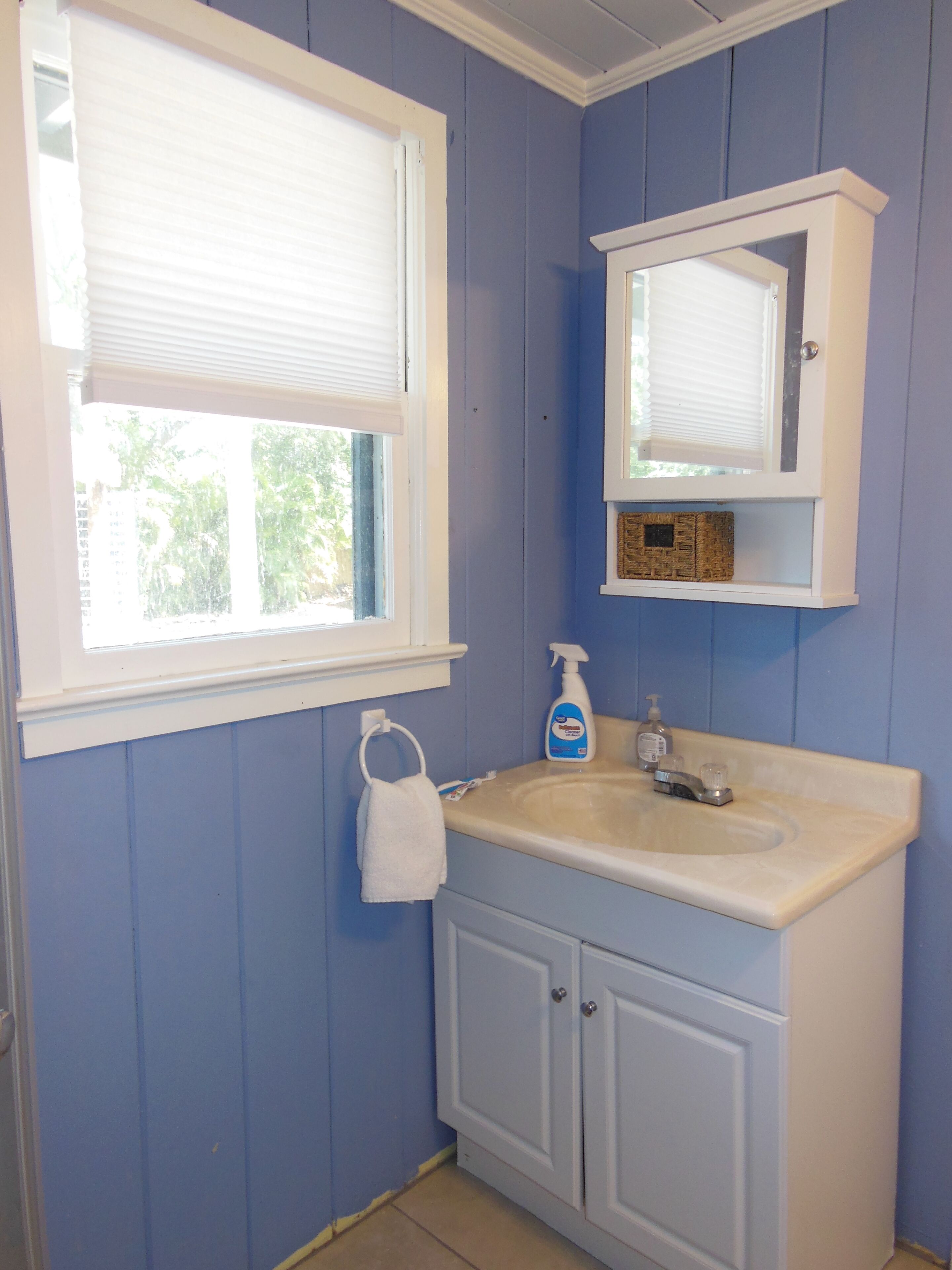 A bathroom with a window, a sink, a mirror, and a towel rack.