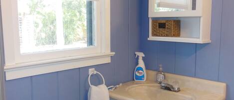 A bathroom with a window, a sink, a mirror, and a towel rack.