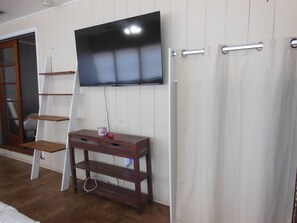 Ein Zimmer mit einem an der Wand montierten Fernseher, einem Holzkonsolentisch, einem weißen Vorhang und einer Holzleiter.