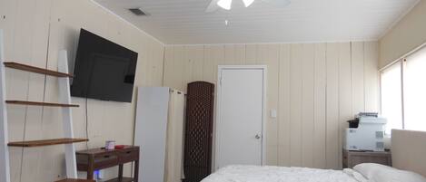 Un dormitorio con cama, escritorio, televisor, puerta y ventilador de techo.