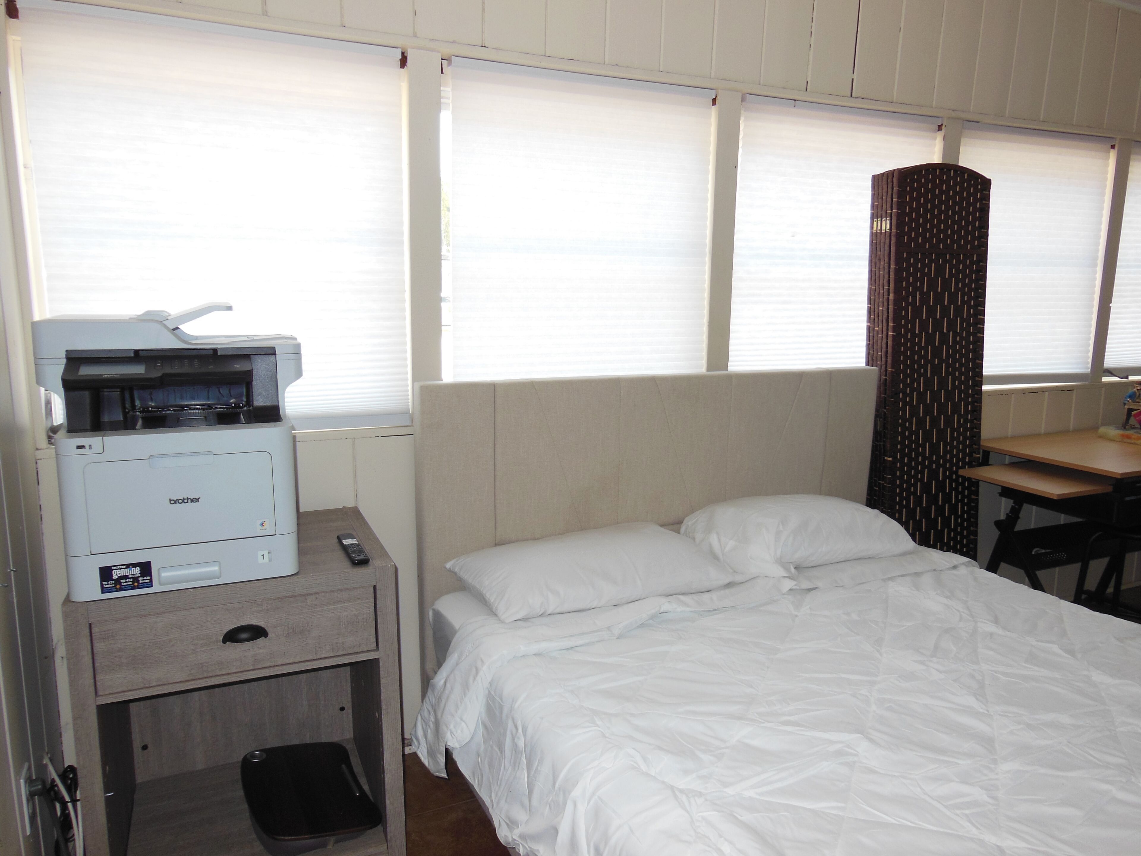 Ein Hotelzimmer mit Bett, Schreibtisch, Drucker und einem Fenster mit Jalousien.
