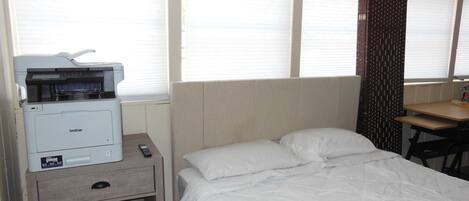 Ein Hotelzimmer mit Bett, Schreibtisch, Drucker und einem Fenster mit Jalousien.
