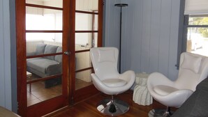A room with a sliding glass door leading to a balcony, two white chairs, a tall floor lamp, and a window with blinds. - Beautiful 2 Bed/2 Bath Cozy Cottage Retreat — Your Home Away From Home (Sarasota)