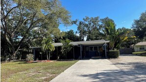 A residential area with a covered porch, a lawn, and trees. - Beautiful 2 Bed/2 Bath Cozy Cottage Retreat — Your Home Away From Home (Sarasota)