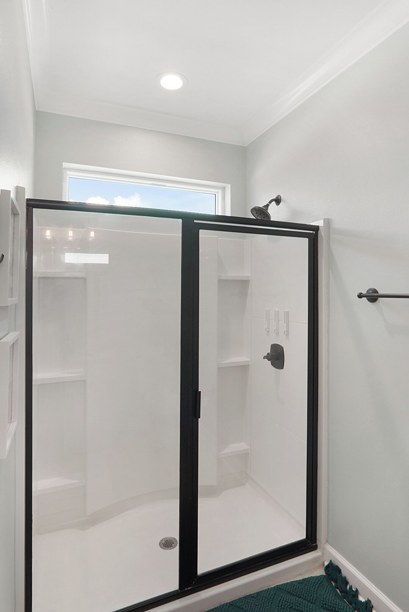 Une douche à l’italienne avec une porte en verre et un cadre noir, une fenêtre au-dessus et un porte-serviettes fixé au mur.