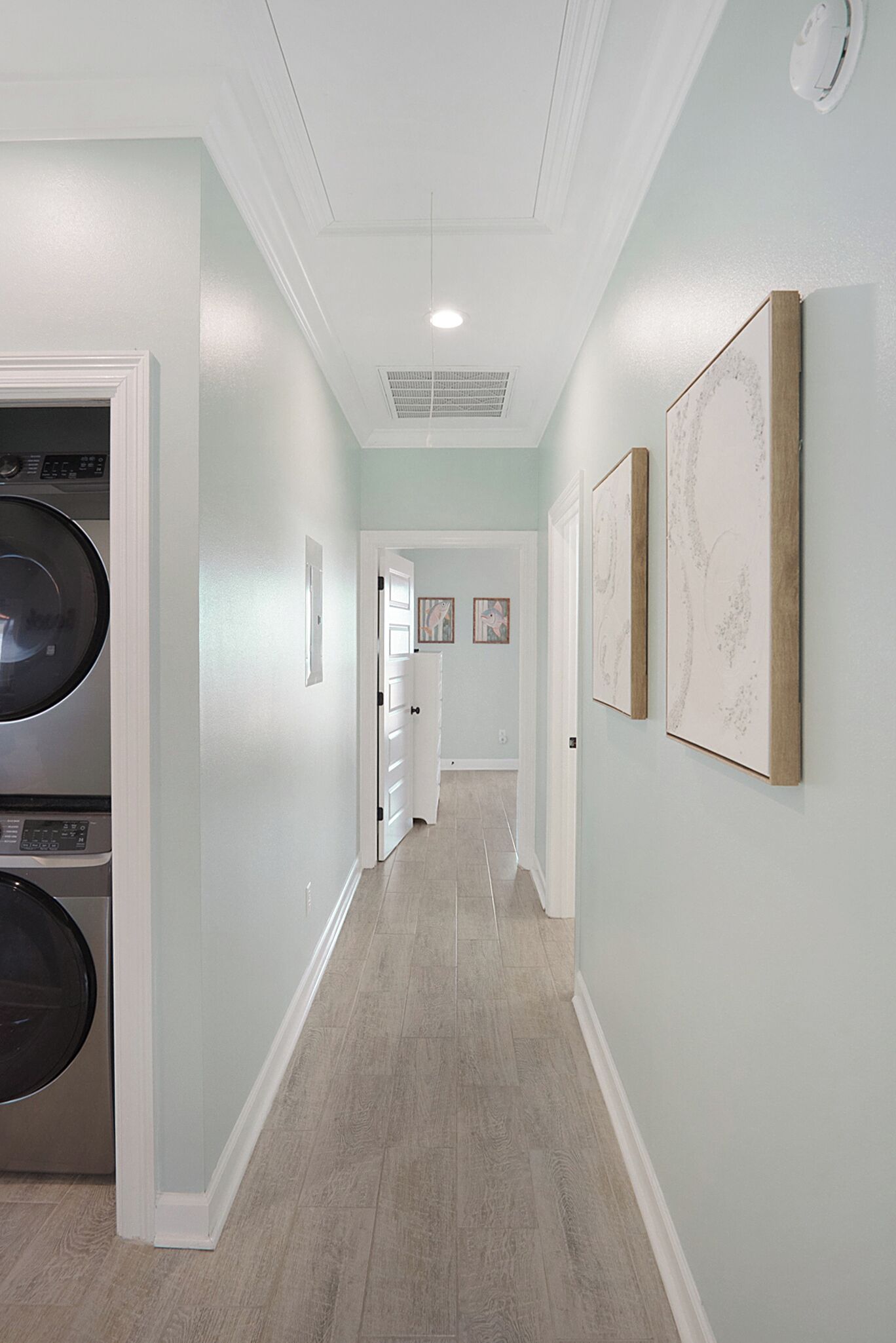 A hallway with a washing machine, a door leading to another room, and framed artwork on the wall.