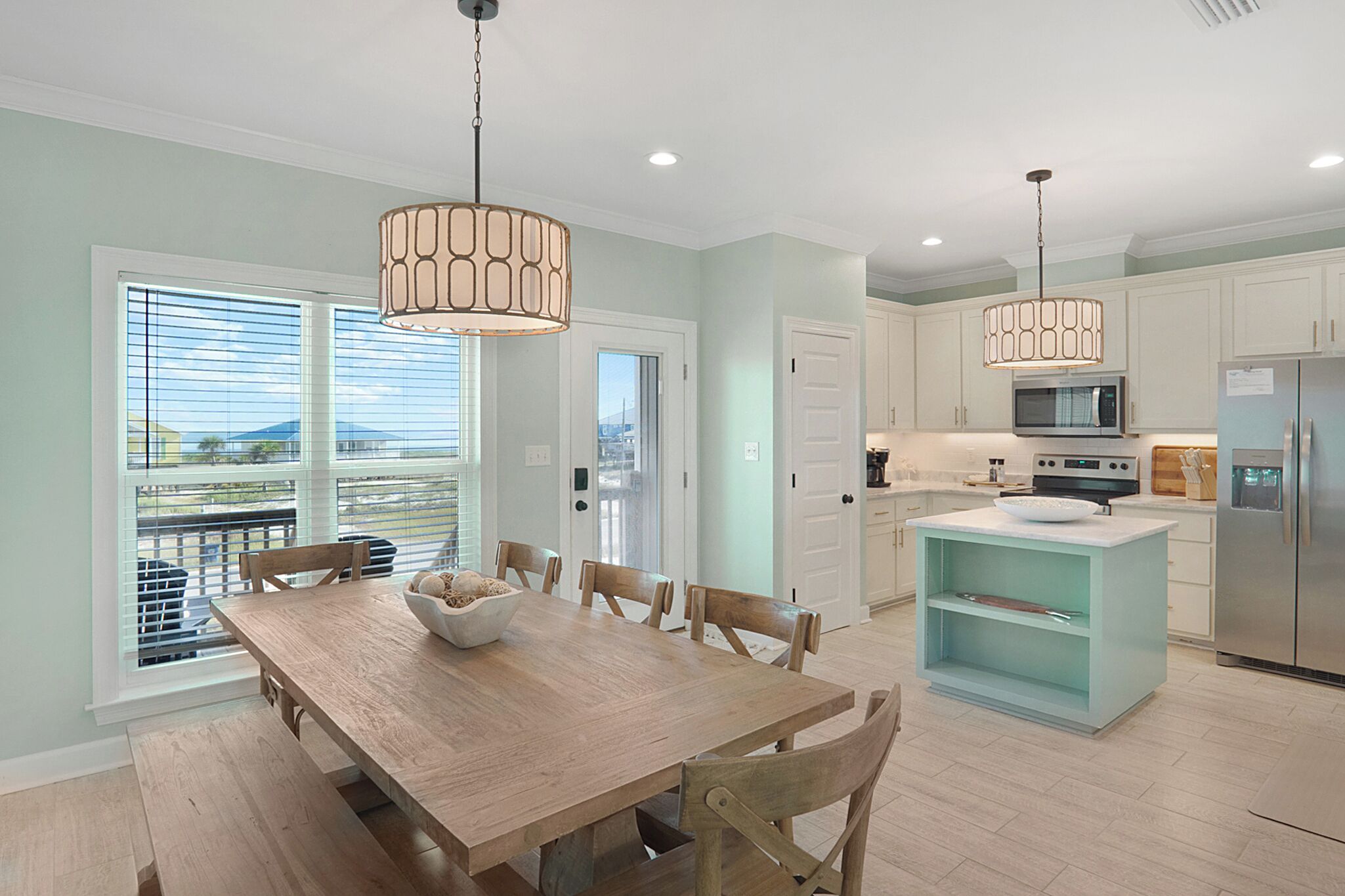 A modern kitchen with a dining area, featuring a wooden table, chairs, a central island, and pendant lighting.