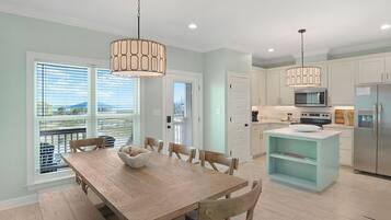 A modern kitchen with a dining area, featuring a wooden table, chairs, a central island, and pendant lighting.
