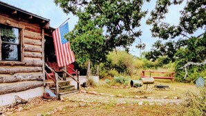 A rustic log cabin with a flag, a porch, and a stone pathway.