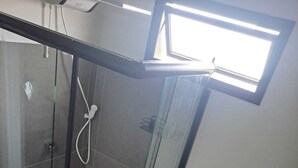 A bathroom with a glass-enclosed shower, a white toilet, and a small window above the toilet. - LU'S HOUSE APARTMENTS (102) (Primavera do Leste)
