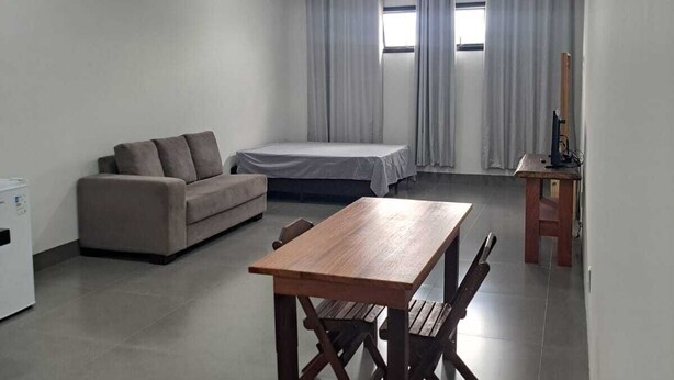 A modern, well-lit room with a wooden table, a sofa, a bed, and a small desk with a chair. - LU'S HOUSE APARTMENTS (102) (Primavera do Leste)