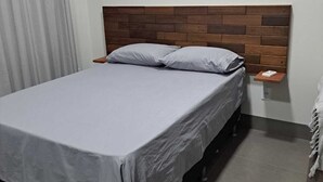 A bed with a wooden headboard, a bedside table, and a nightstand. - LU'S HOUSE APARTMENTS (102) (Primavera do Leste)