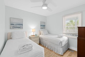 Ein Schlafzimmer mit zwei Betten, einem Deckenventilator, einem Nachttisch mit Lampe und einem Fenster mit Jalousien.