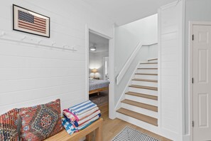 Ein Flur mit Treppe, einem Bett im Hintergrund und einer Wand mit einem gerahmten Wimpel.