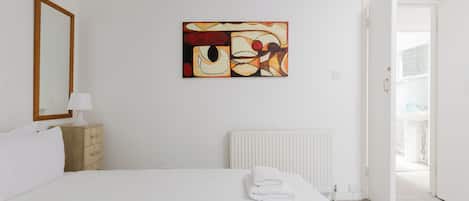 A hotel room with a bed, a radiator, a painting, a wooden dresser, and a door leading to a balcony.