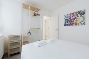 Un dormitorio con cama, cómoda de madera, armario y un cuadro abstracto colorido en la pared.
