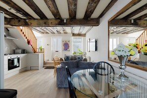 Eine moderne Küche mit Mikrowelle, Herd und Schränken. Ein Essbereich mit Glastisch und Stühlen ist vorhanden. Im Wohnzimmer befinden sich eine Couch und ein Sessel.