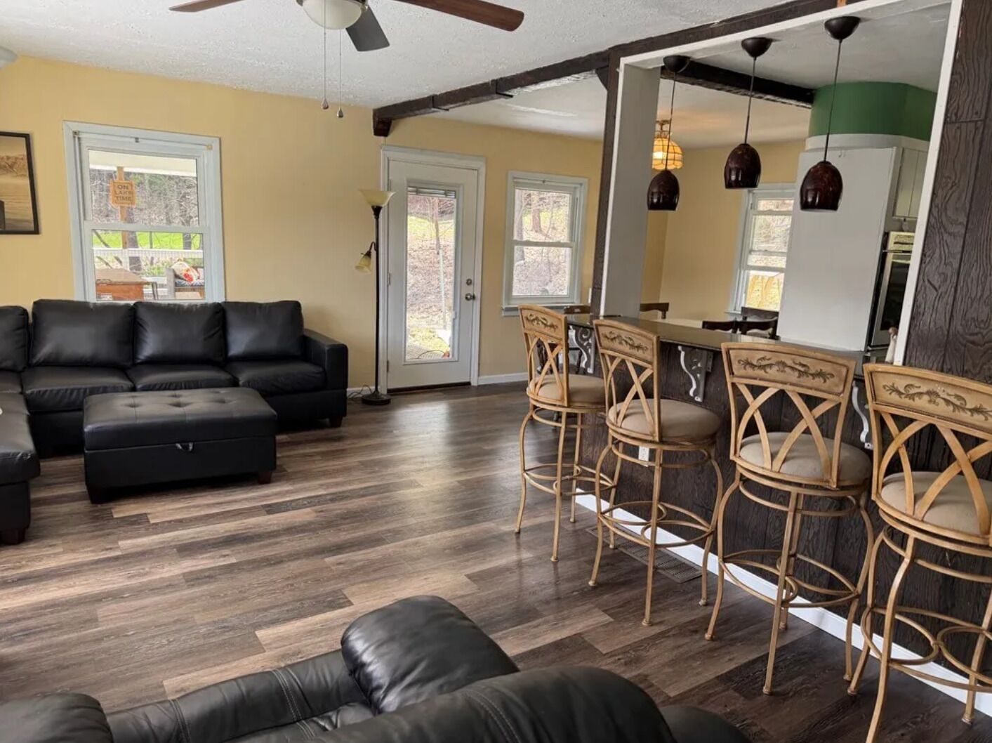 A living room with a sectional sofa, a dining area with bar stools, and a kitchen with pendant lights.