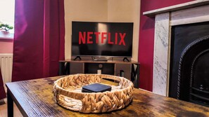 Una sala de estar con un televisor montado en la pared, una chimenea y una cesta tejida sobre una mesa de madera.