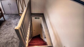 Una escalera alfombrada con un cartel de salida de incendios, una silla de madera y una puerta al fondo.