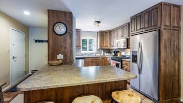 A kitchen with a central island, wooden cabinets, stainless steel appliances, and a clock on the wall.