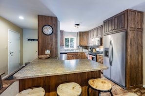 A kitchen with a central island, wooden cabinets, stainless steel appliances, and a clock on the wall.