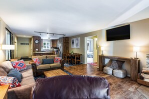 A modern living room with a sofa, coffee table, and fireplace. There is a dining area with a table and chairs. A kitchen is visible in the background. - Lake Fork - Ski-In / Ski-Out, Gas Stove, Parking (Taos Ski Valley)