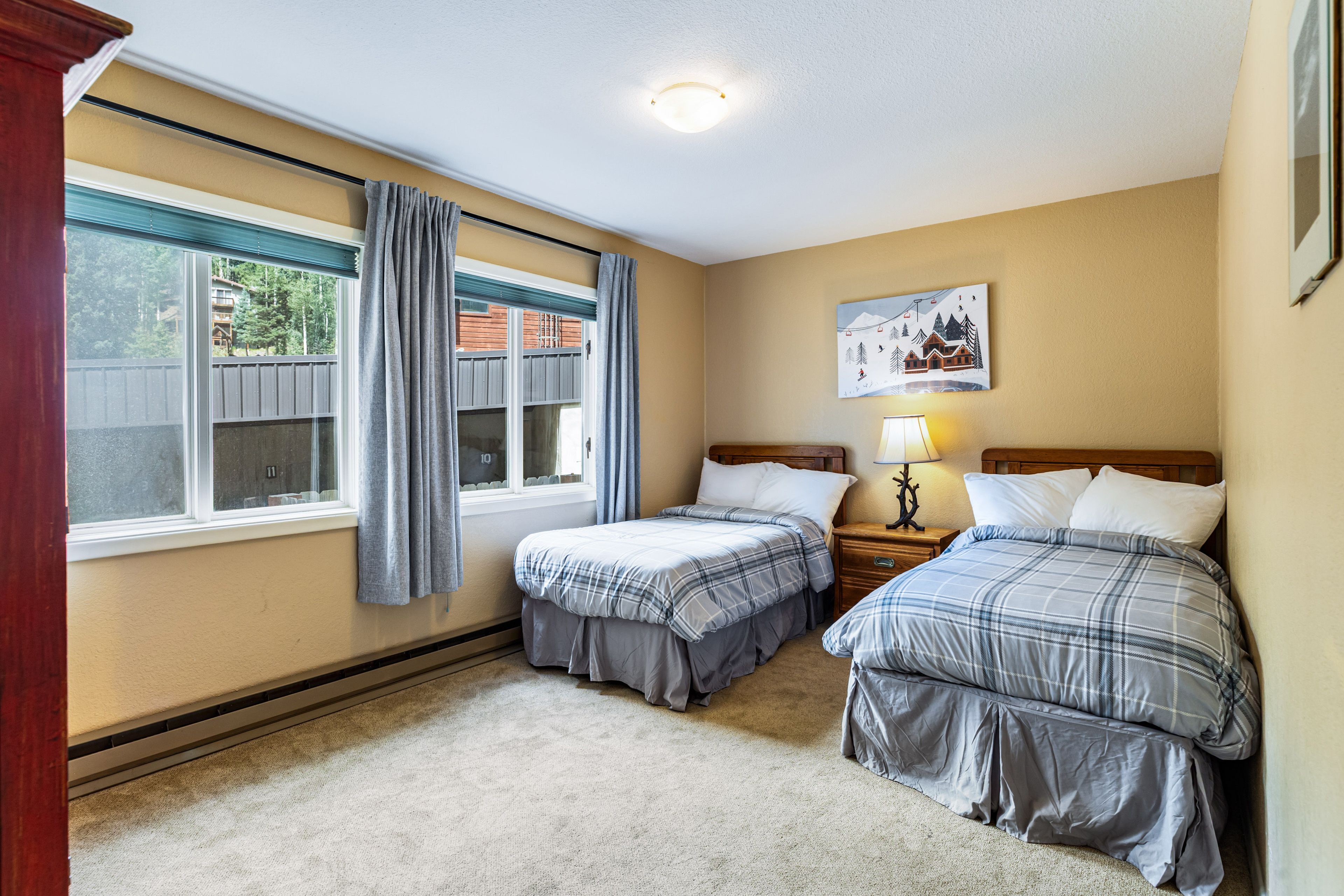 A hotel room with two beds, a window with curtains, a painting on the wall, and a nightstand with a lamp.