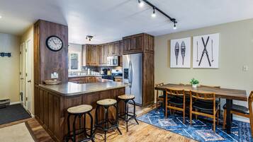 A modern kitchen with wooden cabinets, a stainless steel refrigerator, and a bar area with stools.