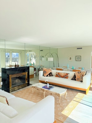 Ein modernes Wohnzimmer mit Kamin, weißem Sofa und Essbereich mit Tisch und Stühlen.