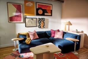 Un salon avec un canapé bleu, deux tables d’appoint, une table basse et des œuvres d’art murales.