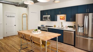 A modern kitchen with dark blue cabinets, stainless steel appliances, and a wooden dining table with bar stools. - Cozy + Quiet, Moon Studio on the Atlanta Beltline. Everything you want. (Atlanta)