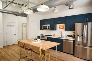A modern kitchen with dark blue cabinets, stainless steel appliances, and a wooden dining table with bar stools. - Cozy + Quiet, Moon Studio on the Atlanta Beltline. Everything you want. (Atlanta)