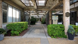 A covered walkway with concrete pillars, glass doors, and potted plants. - Cozy + Quiet, Moon Studio on the Atlanta Beltline. Everything you want. (Atlanta)
