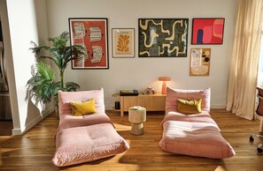 Une pièce avec deux fauteuils roses, un plancher en bois, une plante et une œuvre d’art abstraite accrochée au mur.