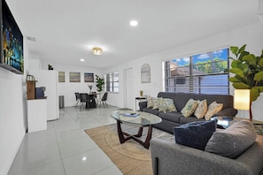 A modern living room with a glass coffee table, a sofa with patterned cushions, a dining area with chairs, and a kitchen area. - PRIVATE TROPICAL RETREAT  JACUZZI, TIKI HUT & OUTDOOR PARADISE (Homestead)