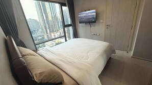 A hotel room with a large bed, a TV mounted on the wall, and a view of tall buildings through the window. - Luxurious 1-bedroom Apartment Near BTS Thonglor, Bangkok (Bangkok)