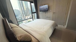 Ein Hotelzimmer mit einem großen Bett, einem an der Wand befestigten Fernseher und Blick auf hohe Gebäude durch das Fenster.