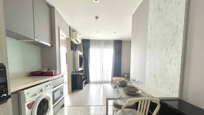 A compact kitchen with a washing machine, a dining area with a table and chairs, and a view of the outside through a window. - Luxurious 1-bedroom Apartment Near BTS Thonglor, Bangkok (Bangkok)