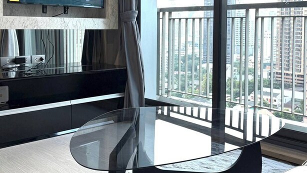 A hotel room with a large window, a flat-screen TV, a glass table, a sofa, and a balcony with a railing. - Luxurious 1-bedroom Apartment Near BTS Thonglor, Bangkok (Bangkok)