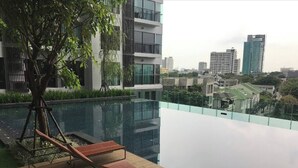 A rooftop pool with lounge chairs, a tree, and a cityscape view. - Luxurious 1-bedroom Apartment Near BTS Thonglor, Bangkok (Bangkok)