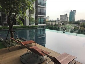 Ein Pool auf dem Dach mit Liegestühlen, einem Baum und Blick auf die Stadt.