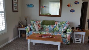 Een woonkamer met een bloemenbank, een houten salontafel, een spiegel en decoratieve vissen aan de muur.
