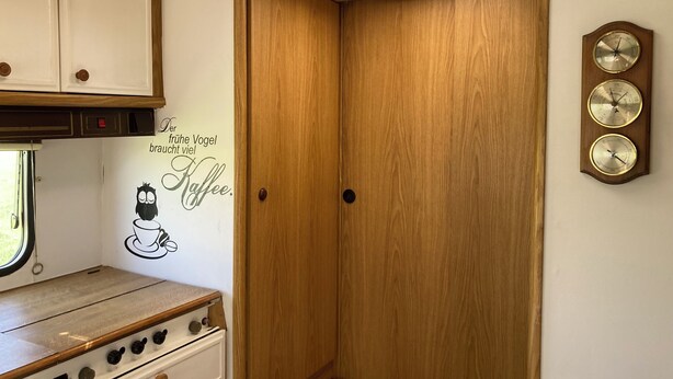 Une cuisine de taille réduite, avec des meubles de rangement en bois, une cuisinière et une horloge murale.
