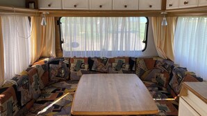 L’intérieur d’un camping-car est aménagé avec une table centrale, des sièges rembourrés, une fenêtre avec des rideaux et des placards situés au-dessus.