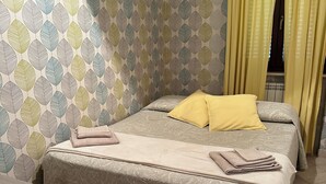 A neatly made bed with a patterned bedspread, a yellow pillow, and folded towels. - In quiet and relaxing setting 1.5km from the sea, suitable for families and friends, (Anzio)