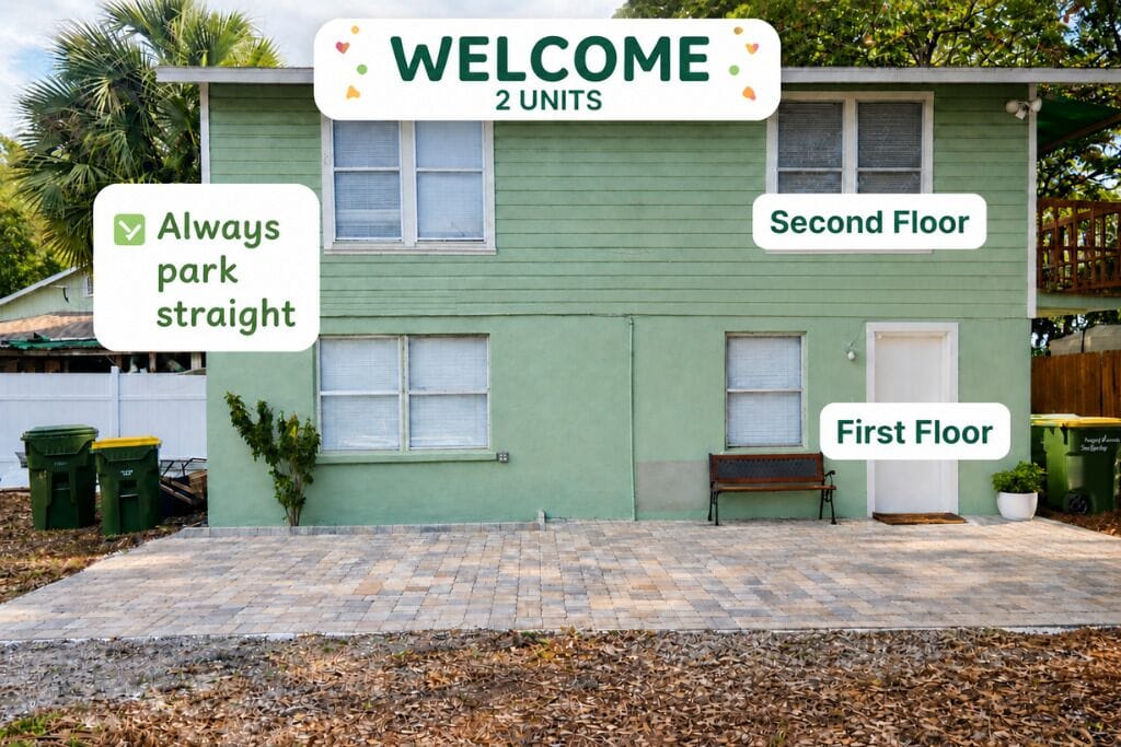 A two-unit house with a green exterior, a paved driveway, and a bench on the first floor.