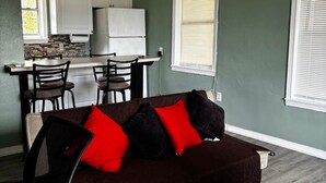A compact living space with a kitchenette, a dining area, and a seating area with a dark brown sofa and red and black cushions. - Downtown Sarasota Rental, 2 Units,4 Bedrooms,3 Baths, Sleeps 10, Lido Beach 6min (Sarasota)